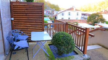 A balcony with a wooden fence, a small table, two chairs, and a potted plant.