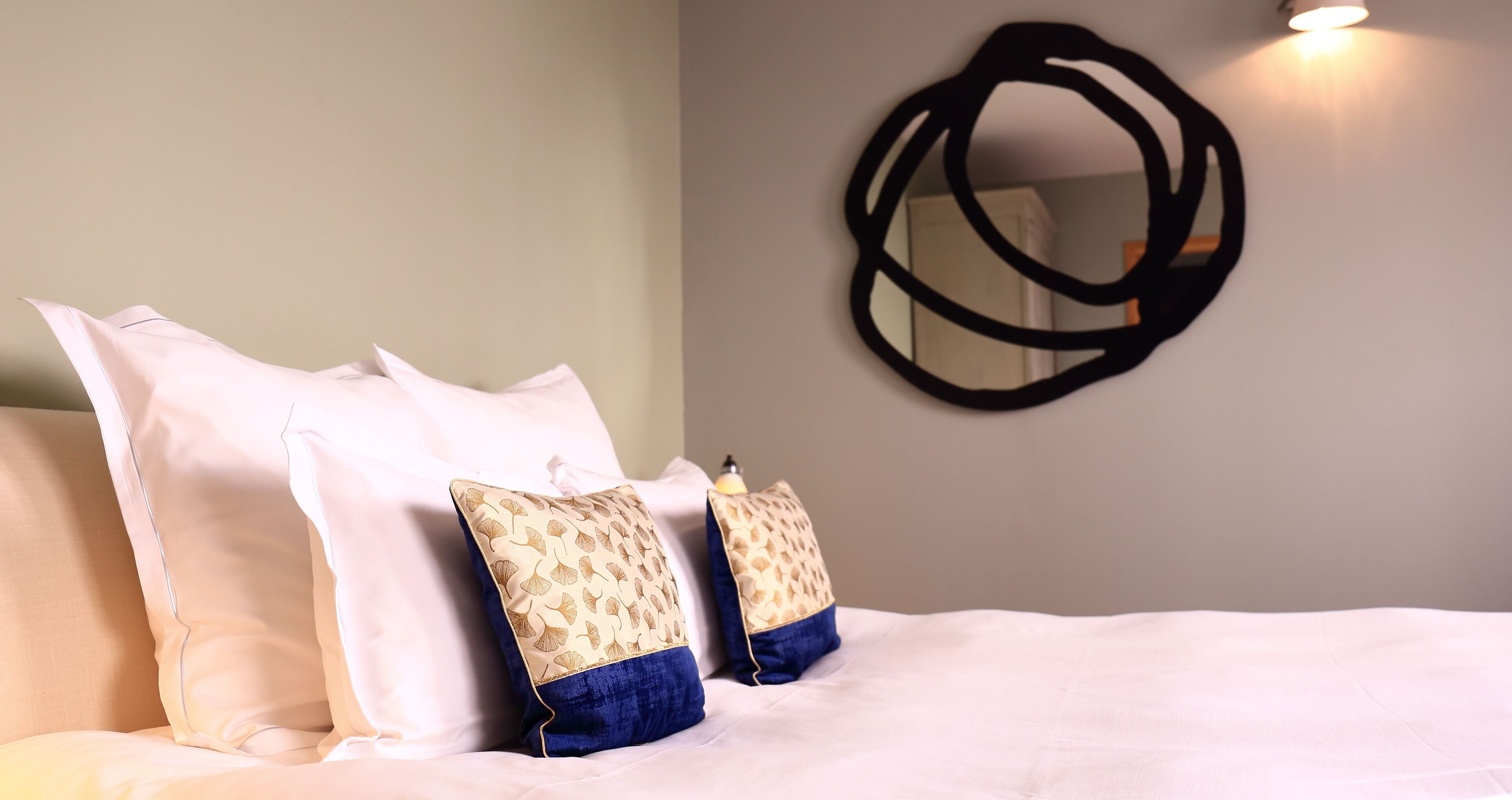 Una cama bien hecha con almohadas blancas y estampadas, una obra de arte abstracto en la pared y una lámpara de noche.