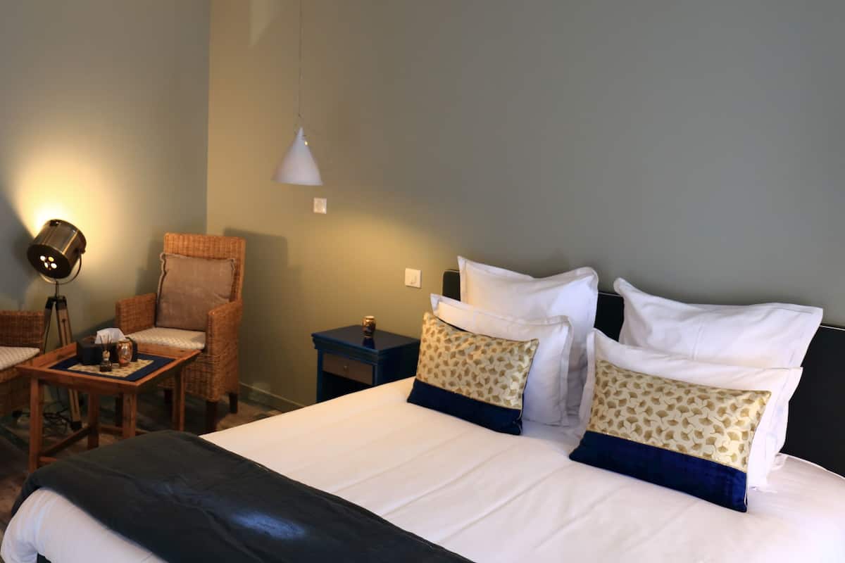 Habitación de hotel con una cama grande, dos sillas, una mesita, una mesita de noche, una lámpara y una bañera.