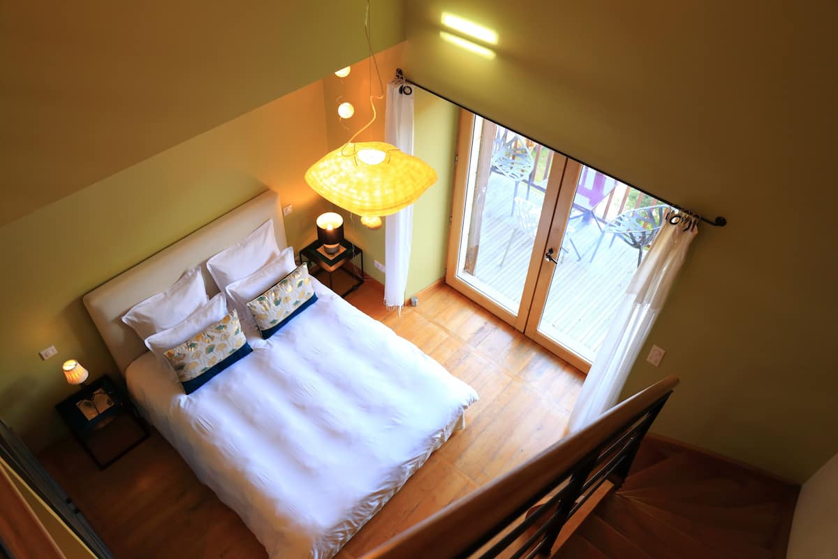 Un dormitorio con una cama, una lámpara de noche y vistas al exterior a través de una ventana.