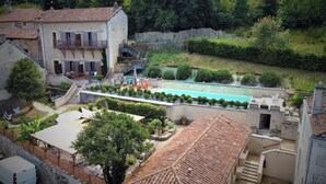 A residential area with a swimming pool, stone buildings, and a staircase leading to a balcony. - Hôtel Restaurant Le Jardin des chouchoux Brantôme  (Brantôme en Périgord)