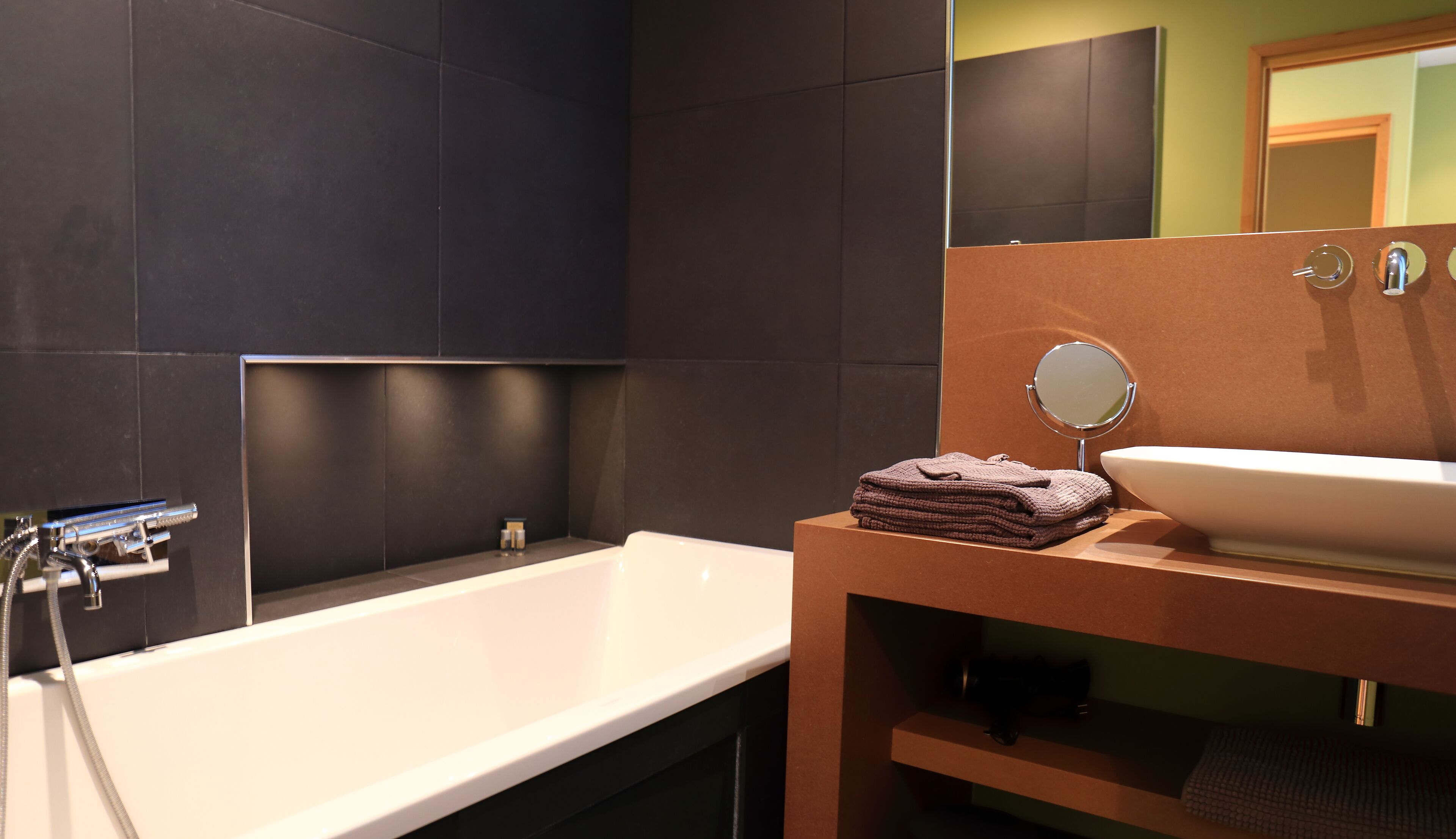 Een moderne badkamer met een witte badkuip, een ronde spiegel en een beige wastafel.