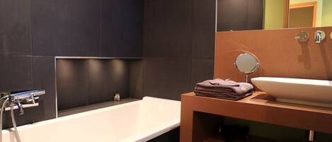 A modern bathroom with a white bathtub, a round mirror, and a beige sink.