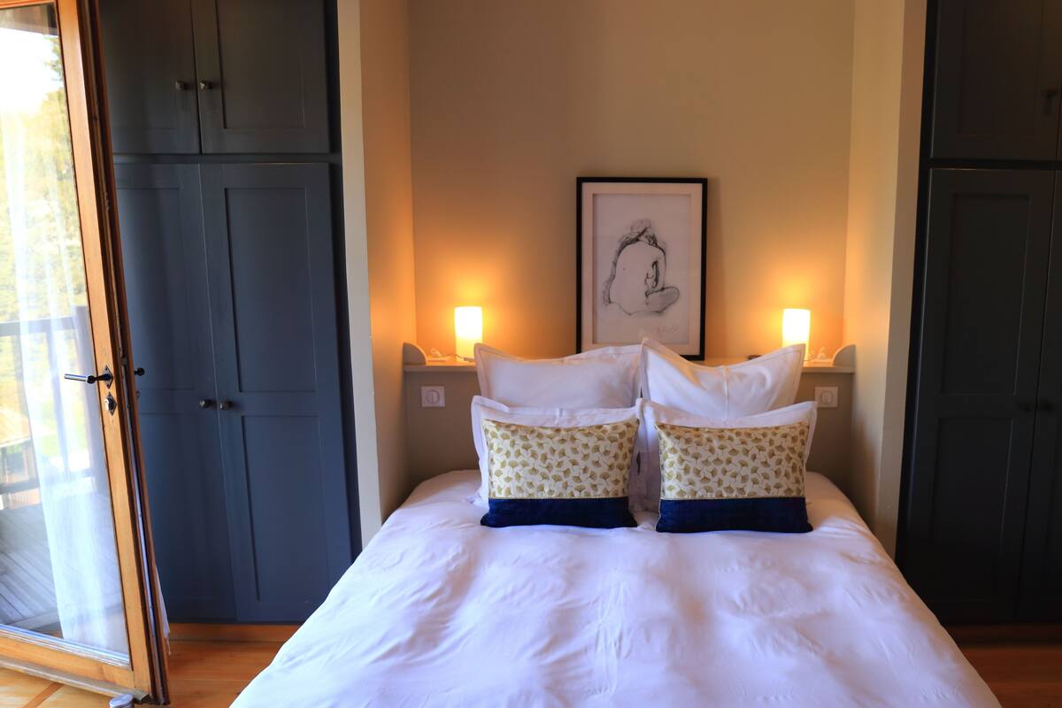Un dormitorio con cama, dos lámparas de noche, una obra de arte enmarcada en la pared y una puerta con vistas al exterior.