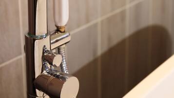 A modern bathroom with a chrome faucet and showerhead, a glass enclosure, and a marble-tiled wall.