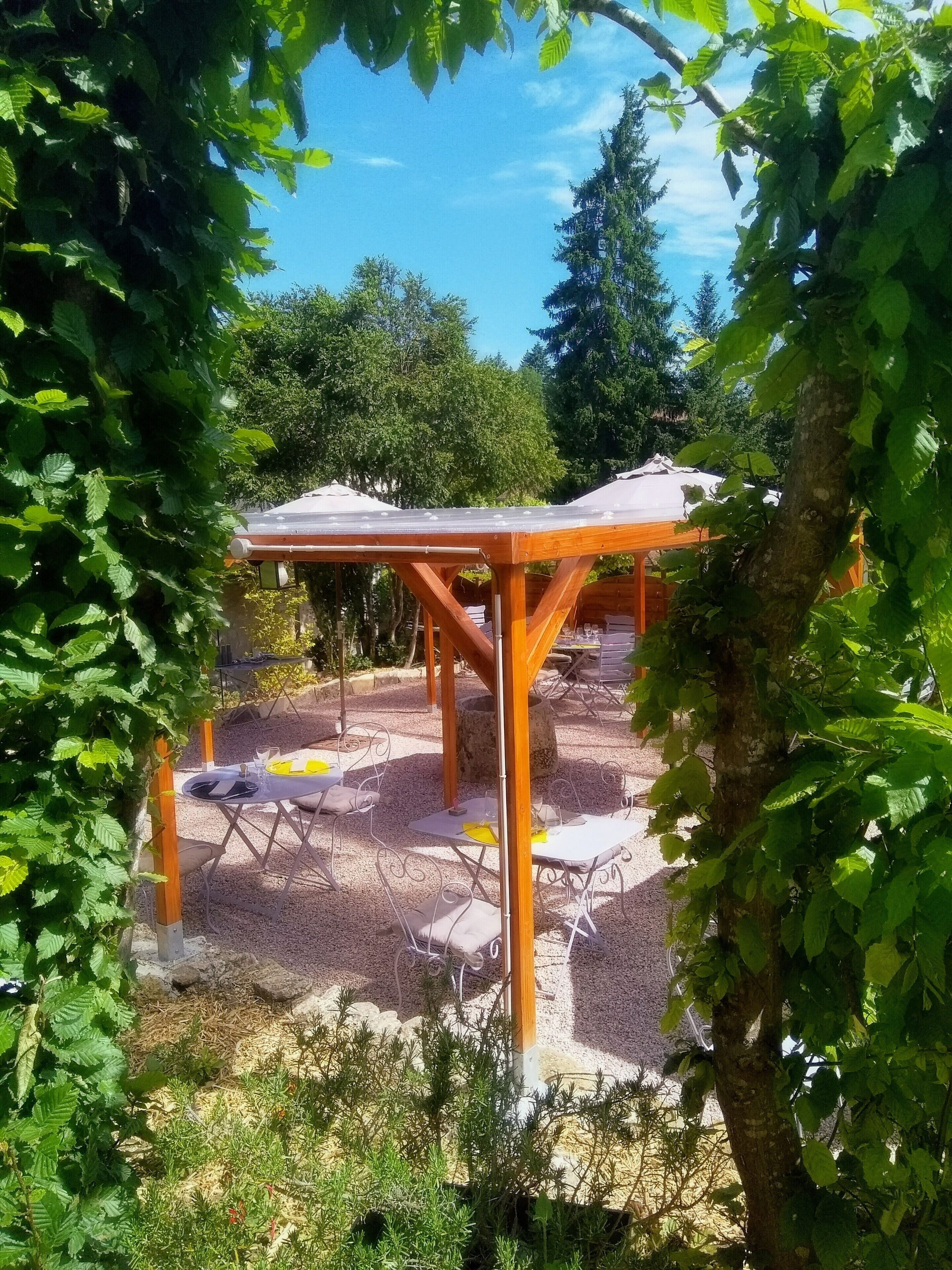 Un espace extérieur aménagé avec des tables et des chaises, entouré de verdure et d’arbres.