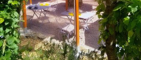 An outdoor seating area with tables and chairs, surrounded by greenery and trees.