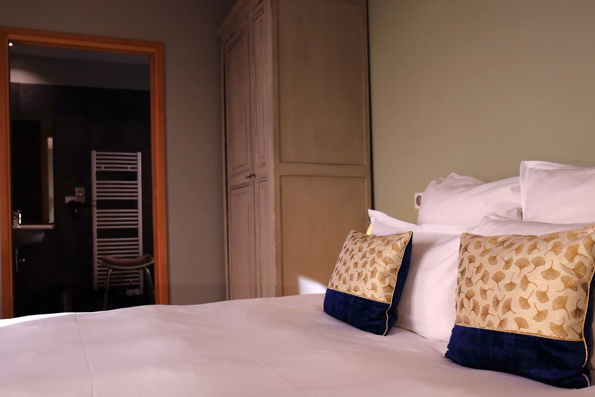 Una cama bien hecha con sábanas blancas y dos almohadones decorativos con diseño de hojas.