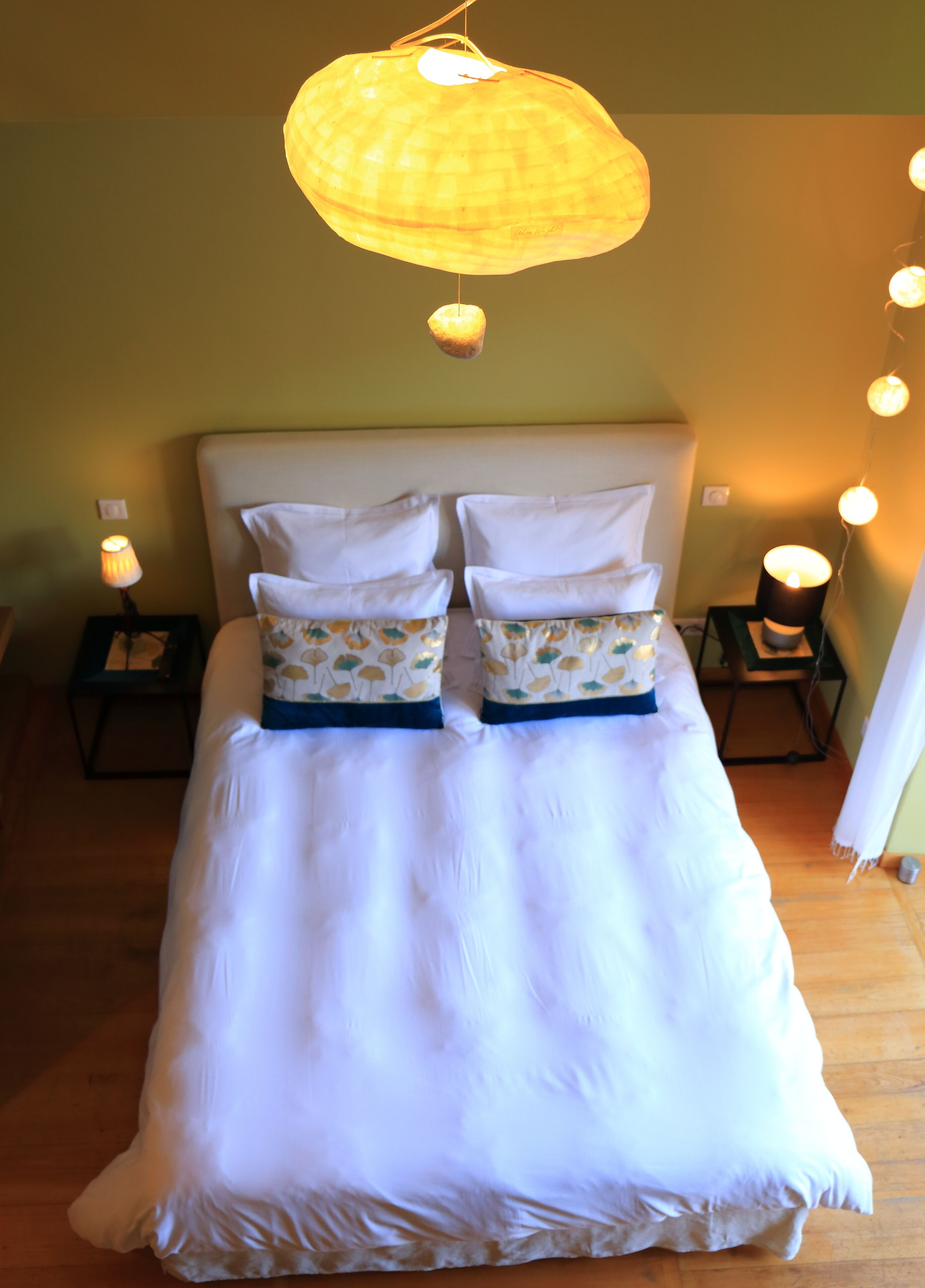 A bed with white bedding and patterned pillows, two bedside tables with lamps, and a hanging light fixture.