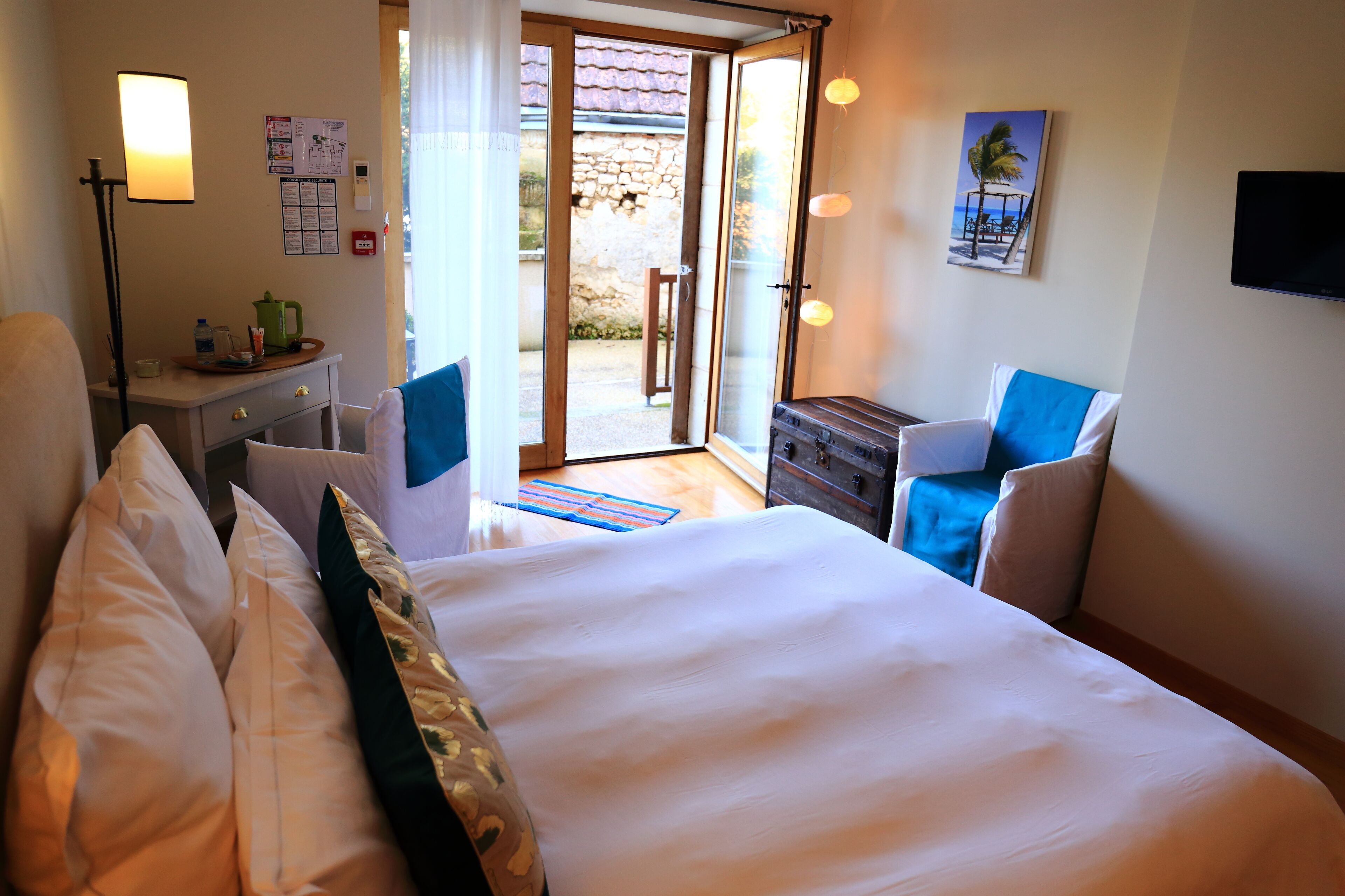 Une chambre d’hôtel avec un lit, un bureau doté d’une lampe, une chaise, une petite table avec une bouilloire et une vue sur l’extérieur.