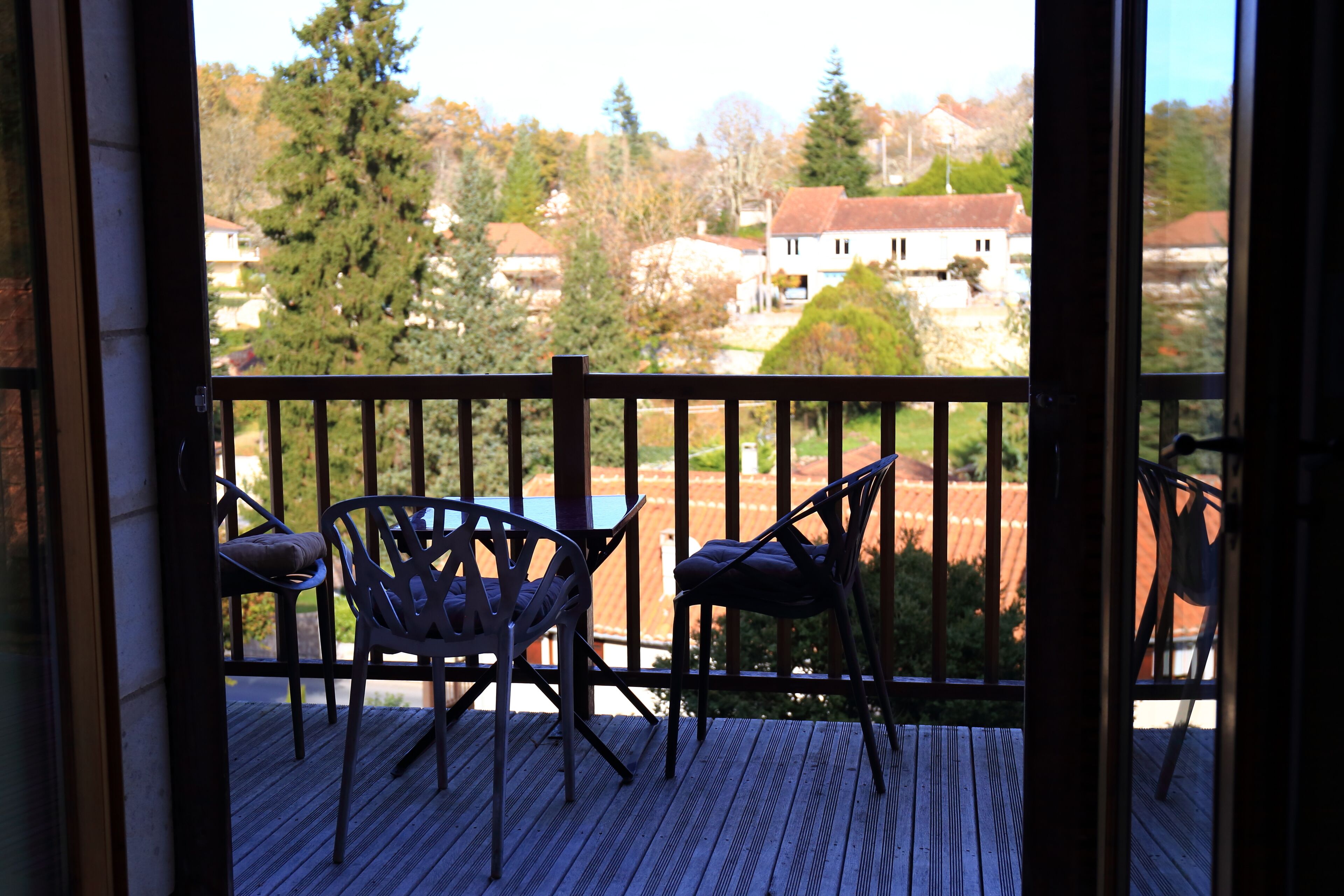 Un balcón con dos sillas y una mesa, con vistas a una zona residencial con casas y árboles.