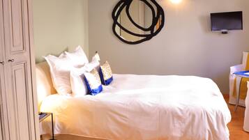 A neatly made bed with white linens and decorative pillows, a wall-mounted TV, and a wooden floor.