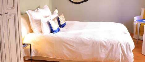 A neatly made bed with white linens and decorative pillows, a wall-mounted TV, and a wooden floor.