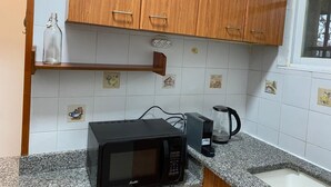 Une cuisine avec des meubles de rangement en bois, un four à micro-ondes, une machine à café et une petite étagère sur laquelle se trouve une bouteille en verre.