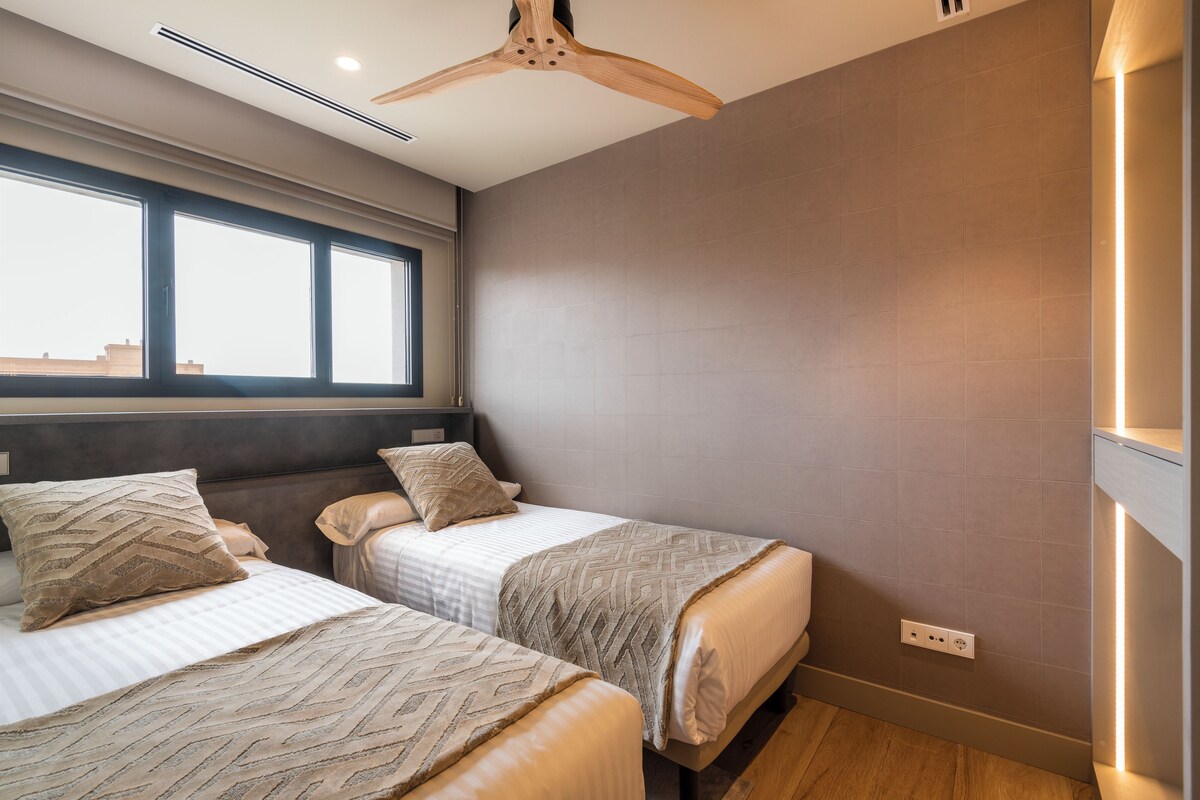 Un dormitorio con dos camas, una ventana, un ventilador de techo y una lámpara en la pared.
