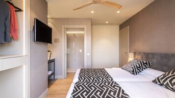 Una habitación de hotel moderna con una cama grande, un ventilador de techo, un televisor montado en la pared y un baño visible a través de una puerta abierta.