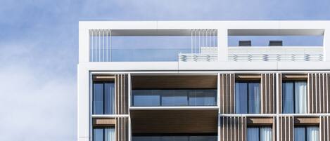Un edificio moderno de varios pisos con techo plano, ventanas grandes y un balcón con barandillas.