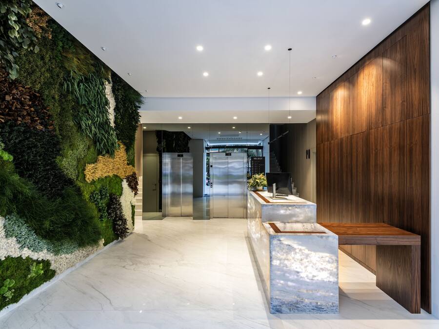 Una zona de recepción moderna con una pared verde, un panel de madera y un suelo de mármol.