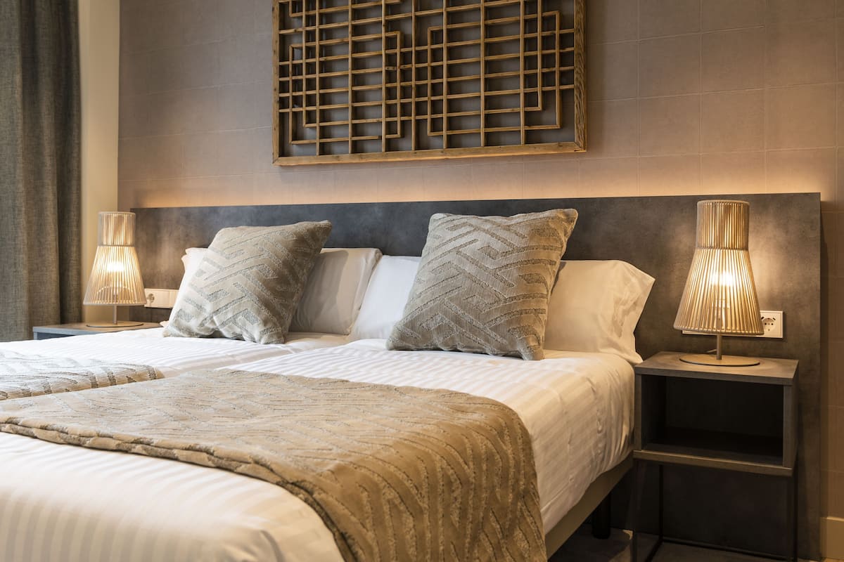 A double bed with a patterned bedspread, two bedside lamps, and a geometric wall decoration.
