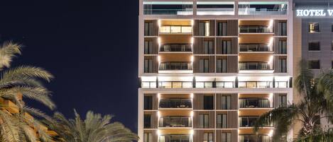 A multi-story hotel with a modern design, featuring balconies on each floor and a prominent "HOTEL V" sign.