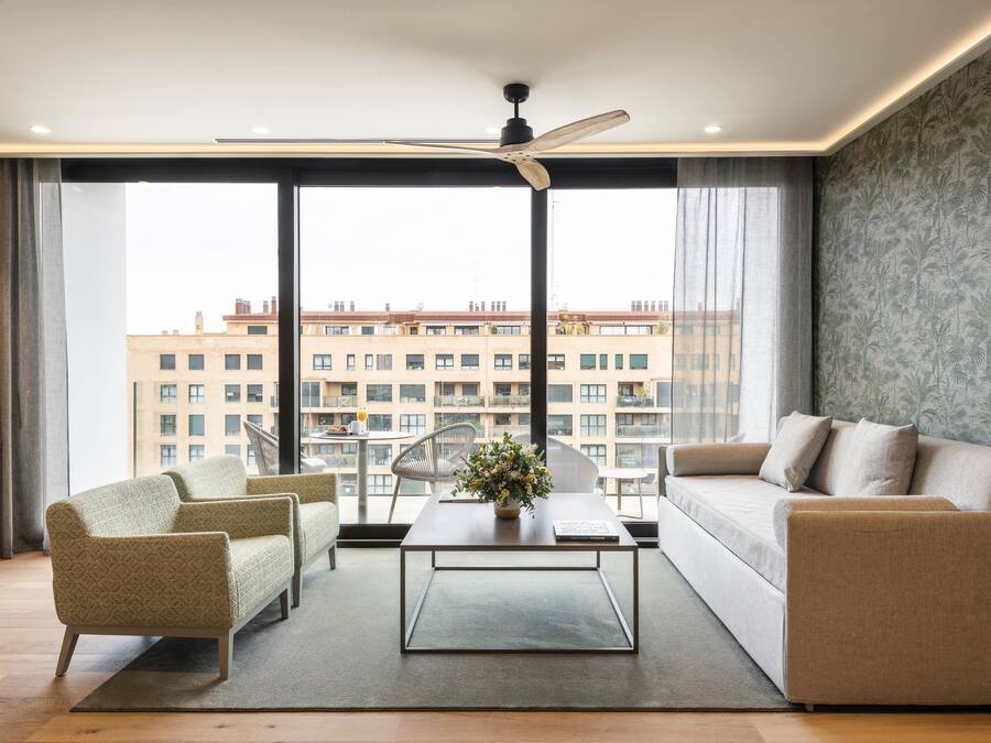Una sala de estar moderna con sofá, sillones, una mesa de centro y vistas de un edificio a través de amplias ventanas.