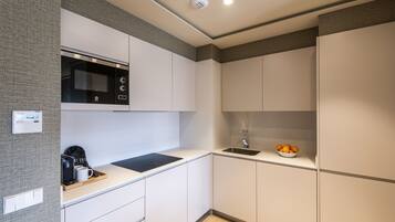 A modern kitchen with white cabinetry, a black microwave, a coffee machine, and a bowl of oranges on the counter.