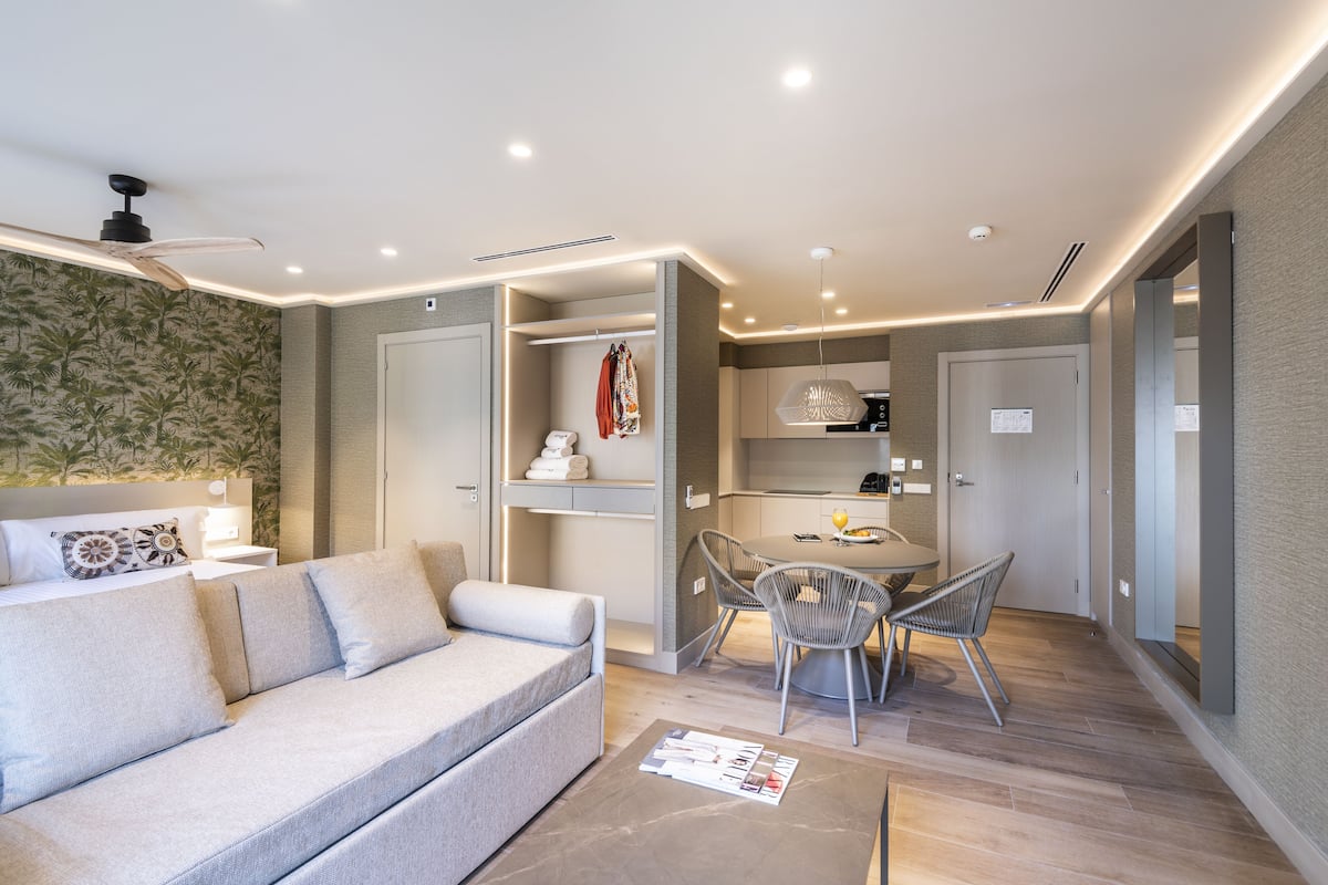 A modern living room with a sofa, a dining table with chairs, a ceiling fan, and a kitchen area.