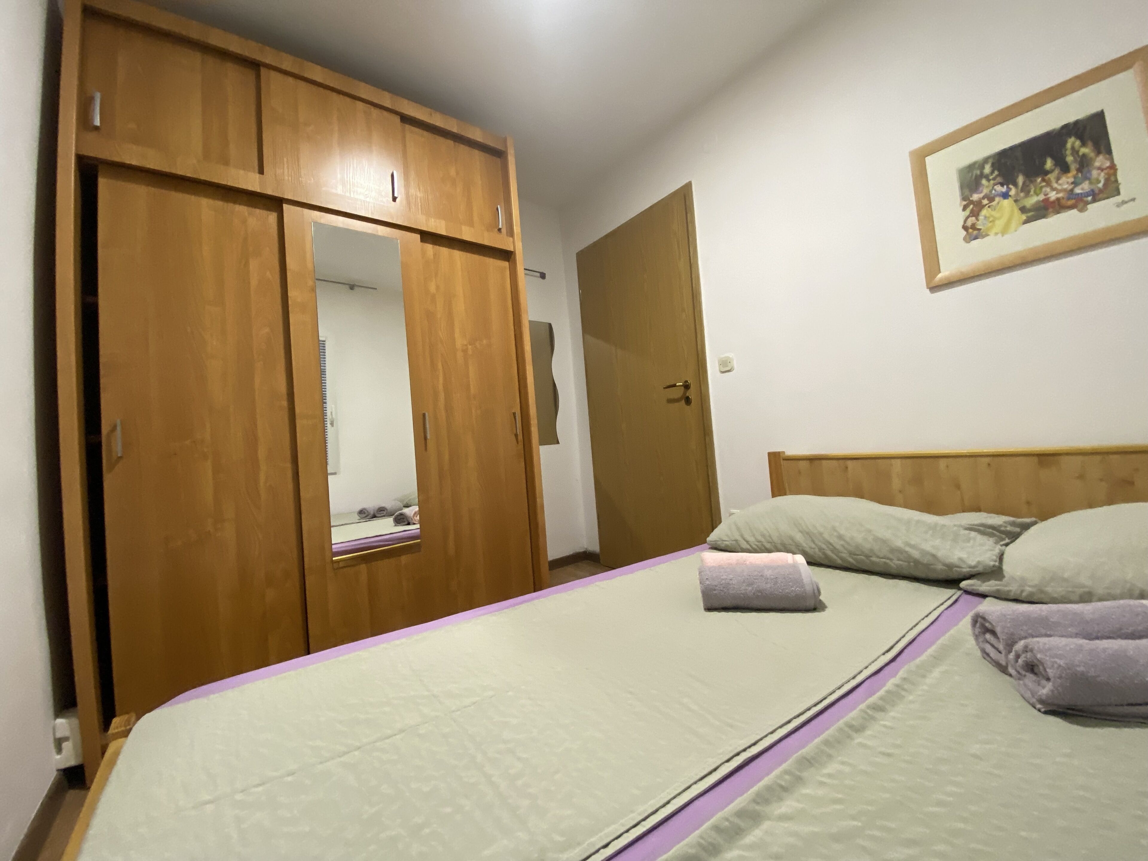 Un dormitorio con cama, armario de madera, puerta y un cuadro en la pared.