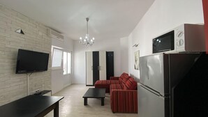 Una sala de estar con televisor de pantalla plana, mesa de comedor, sofá, refrigerador y candelabro.