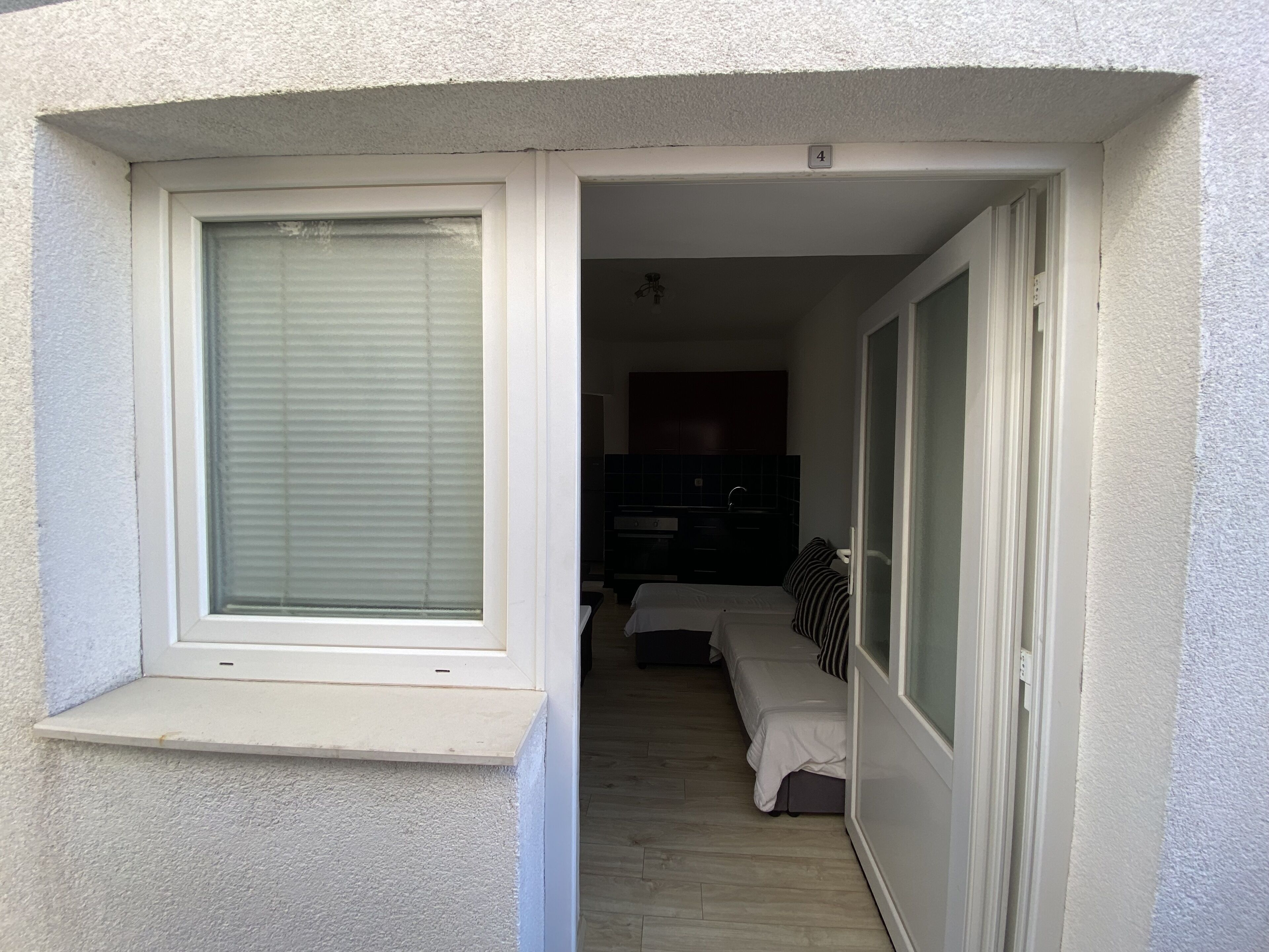 A narrow entryway leading to a bedroom with a window, a door, and a dark-colored dresser.
