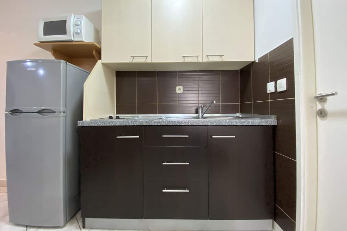 A compact kitchen with dark cabinets, a grey refrigerator, and a microwave on a shelf.