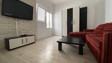 A modern living room with a flat-screen TV mounted on a brick wall, a wooden cabinet, a black coffee table, a red-striped sofa, and a wardrobe with black and white doors.
