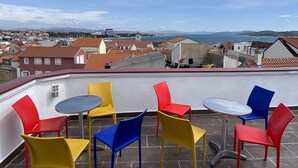 Una terraza con sillas y mesas coloridas con vistas a un pueblo costero.