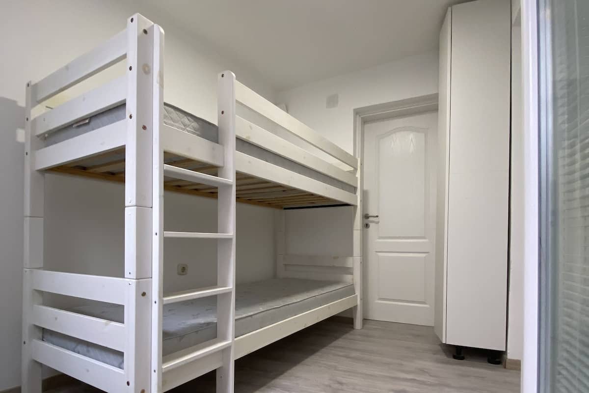 A room with a bunk bed, a door, and a white wardrobe.
