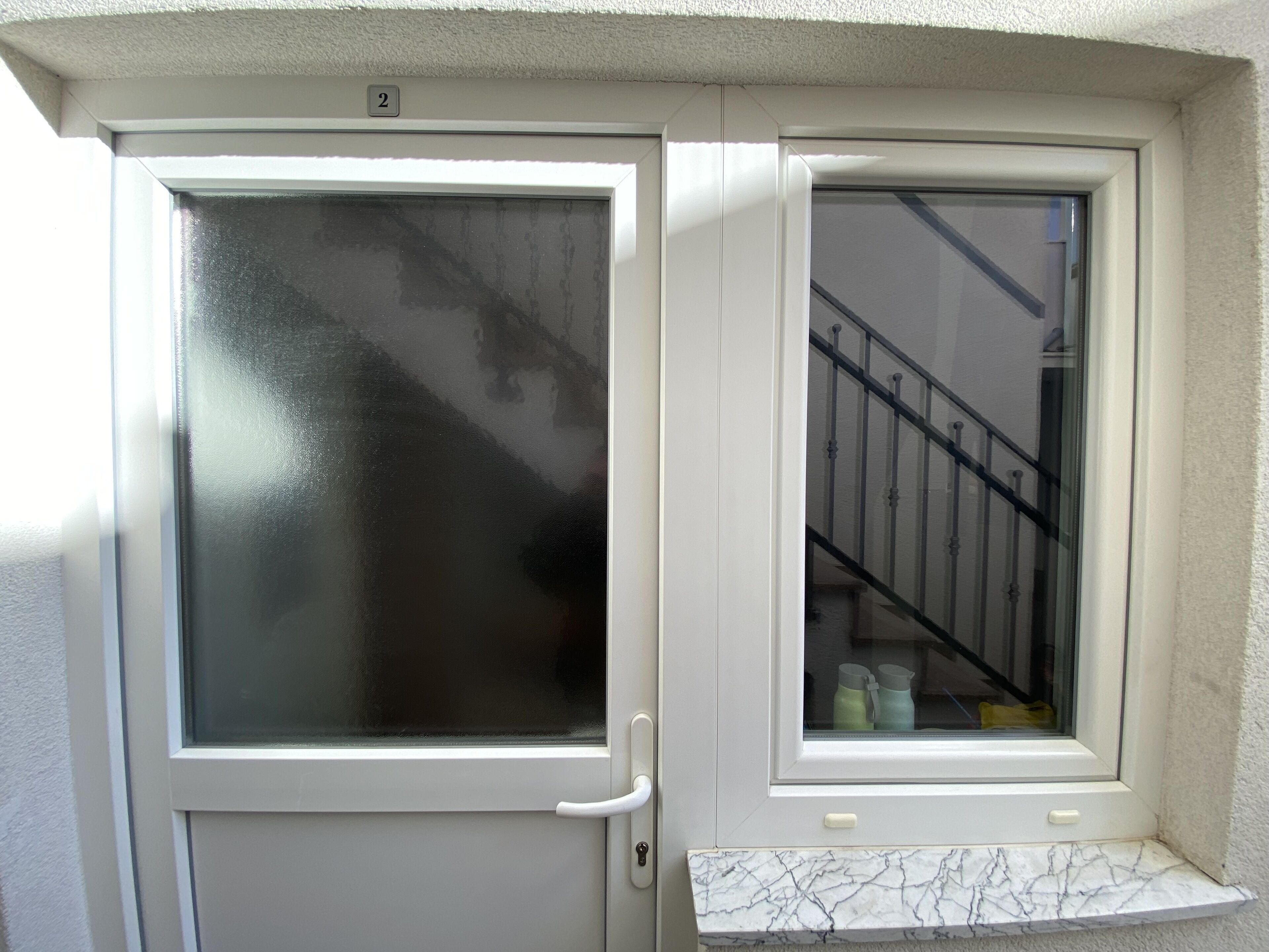 Uma porta branca com painel de vidro fosco e uma pequena janela com um pequeno parapeito de mármore branco abaixo.