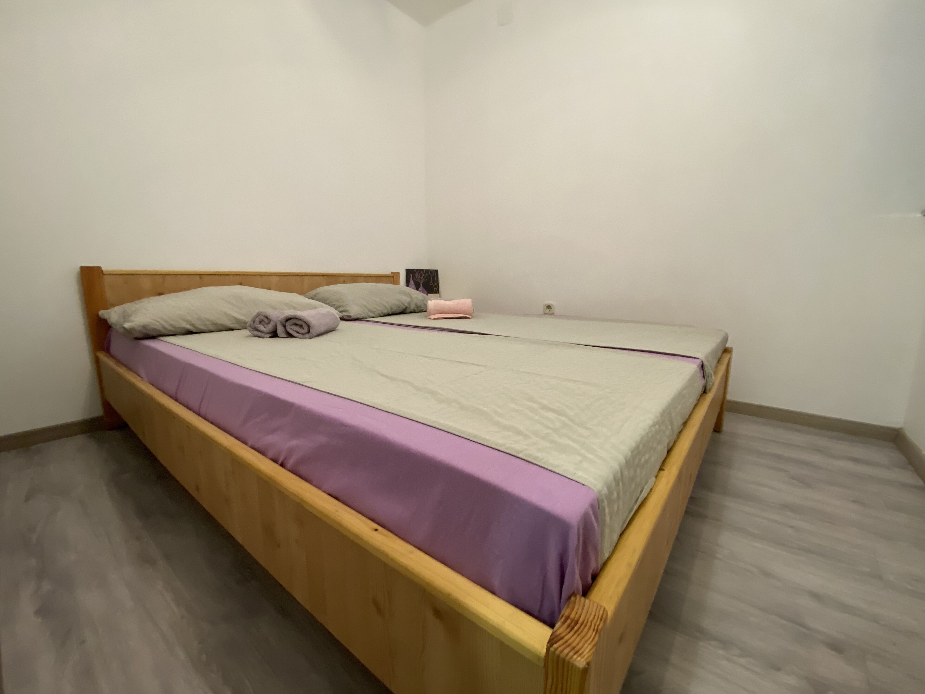 A single bed with a wooden frame, a purple bedspread, and two pillows.