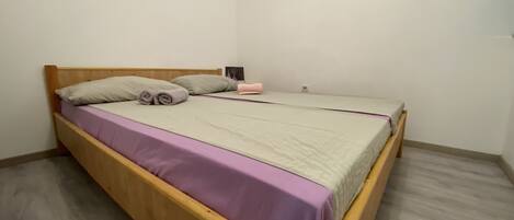 A single bed with a wooden frame, a purple bedspread, and two pillows.