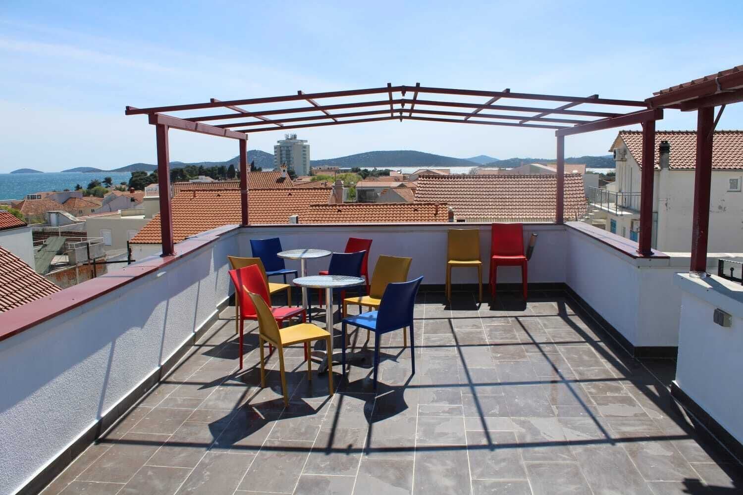 Una terraza en la azotea con pérgola, mobiliario exterior y vistas al mar y edificios.