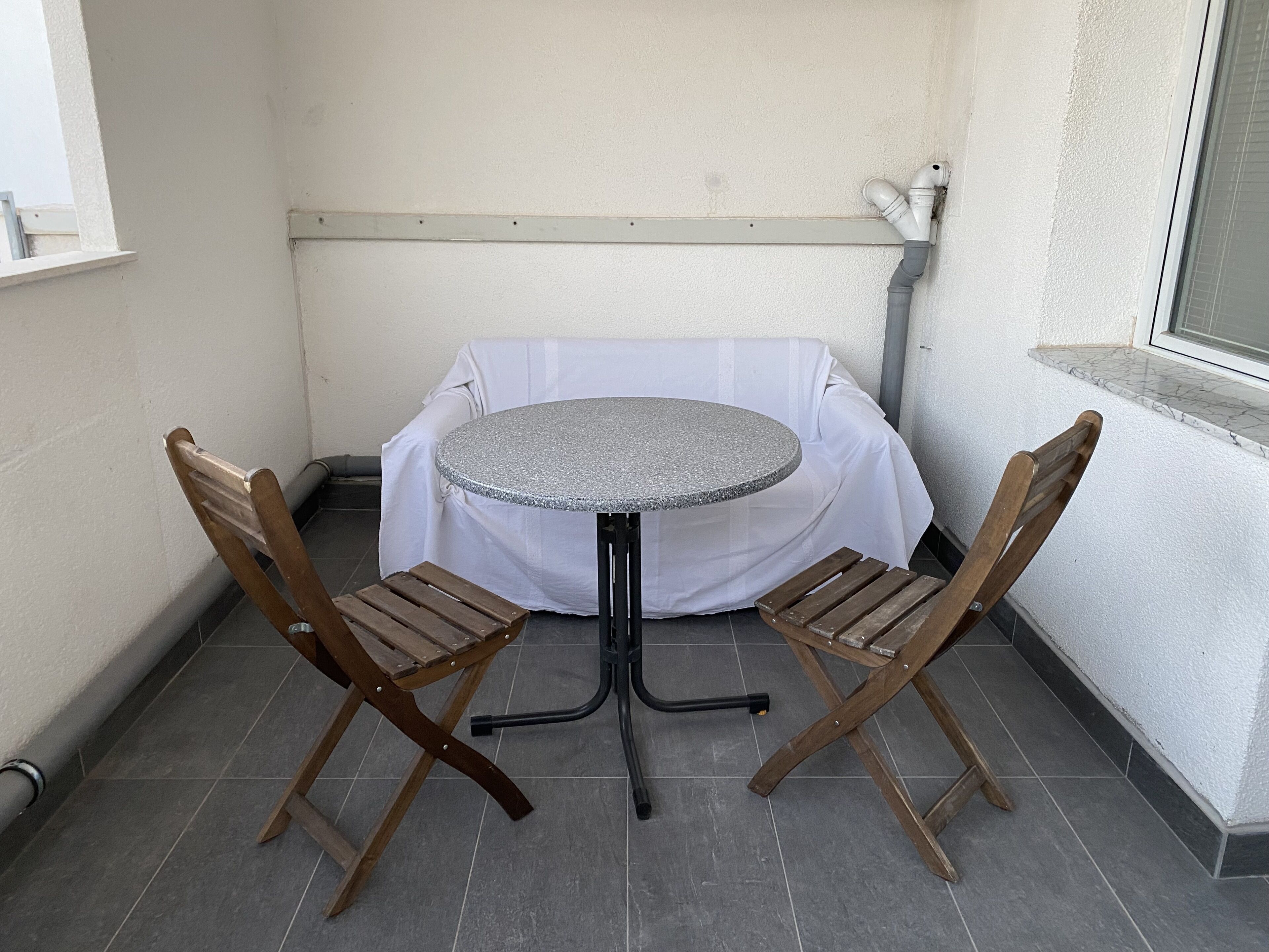 A small outdoor patio with a round table and two wooden chairs, covered by a white tablecloth.