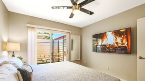 A bedroom with a bed, a ceiling fan, a TV displaying a fire, and a sliding door leading to an outdoor area. - Rustic 2 Bedroom Canyon Suite Biltmore Camelback (Phoenix)
