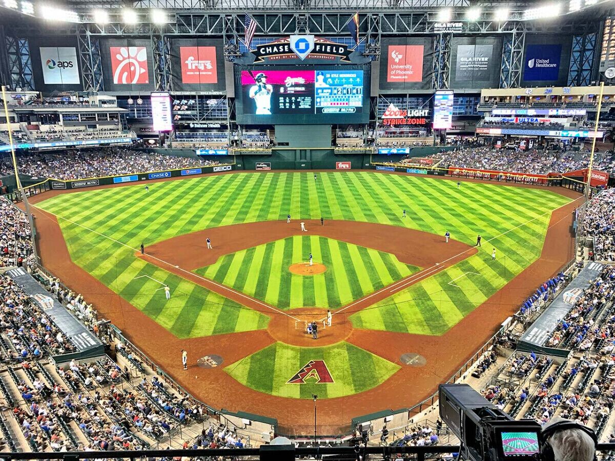 A baseball stadium with a large screen displaying game information, multiple advertising banners, and a well-maintained field.