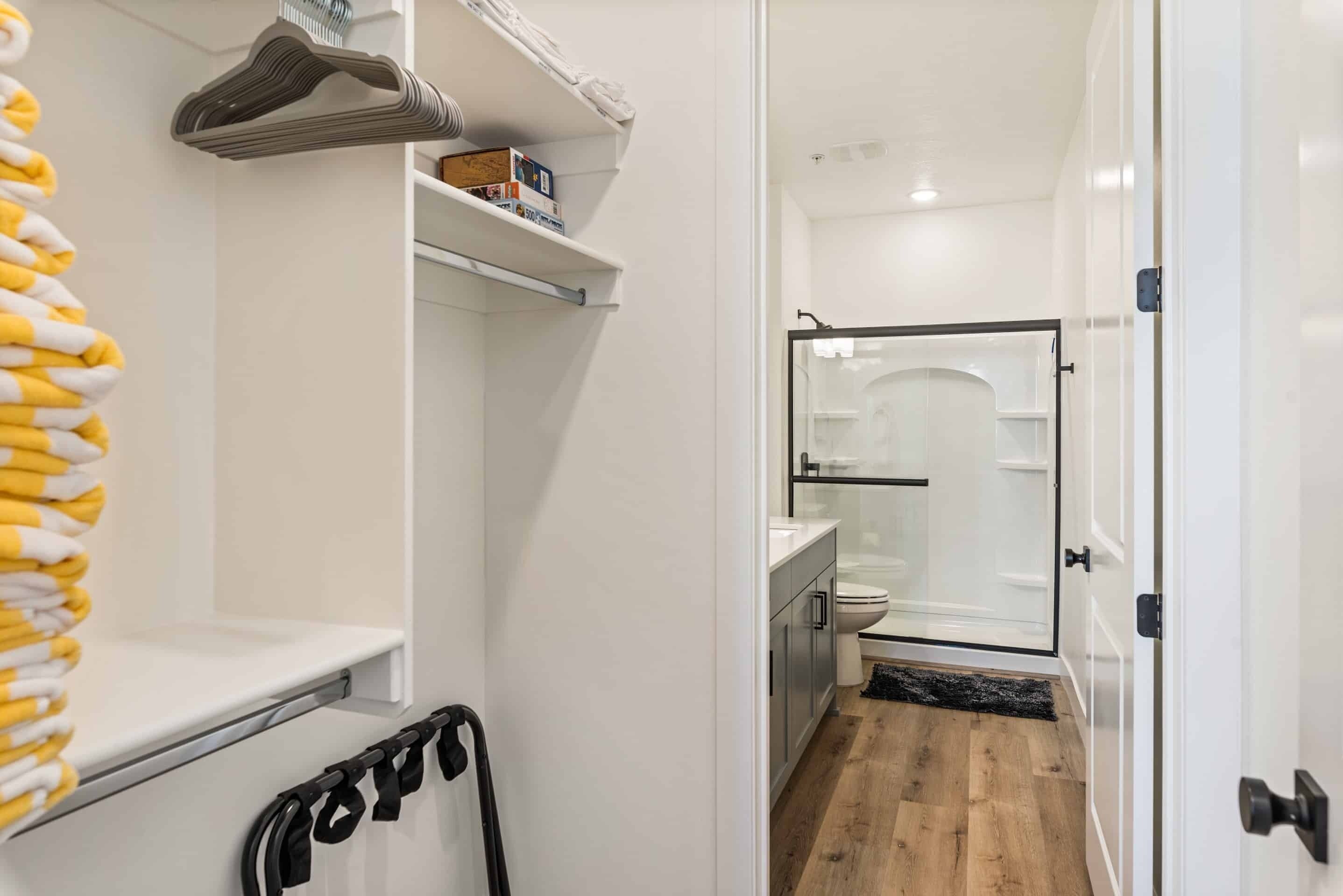A bathroom with a shower, toilet, and sink. There is a towel rack with yellow towels and a black towel on the wall.