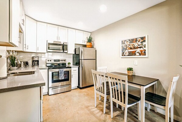 A compact kitchen with white cabinets, stainless steel appliances, and a dining area with white chairs.