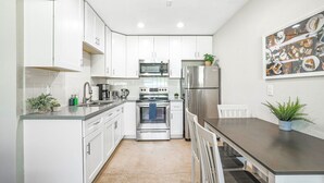 Una cocina moderna con armarios blancos, electrodomésticos de acero inoxidable y un comedor con mesa y sillas.