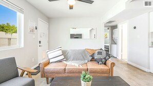 Una sala de estar moderna con un ventilador de techo, un sofá con cojines estampados, una mesa de centro con una planta y un espejo grande en la pared.