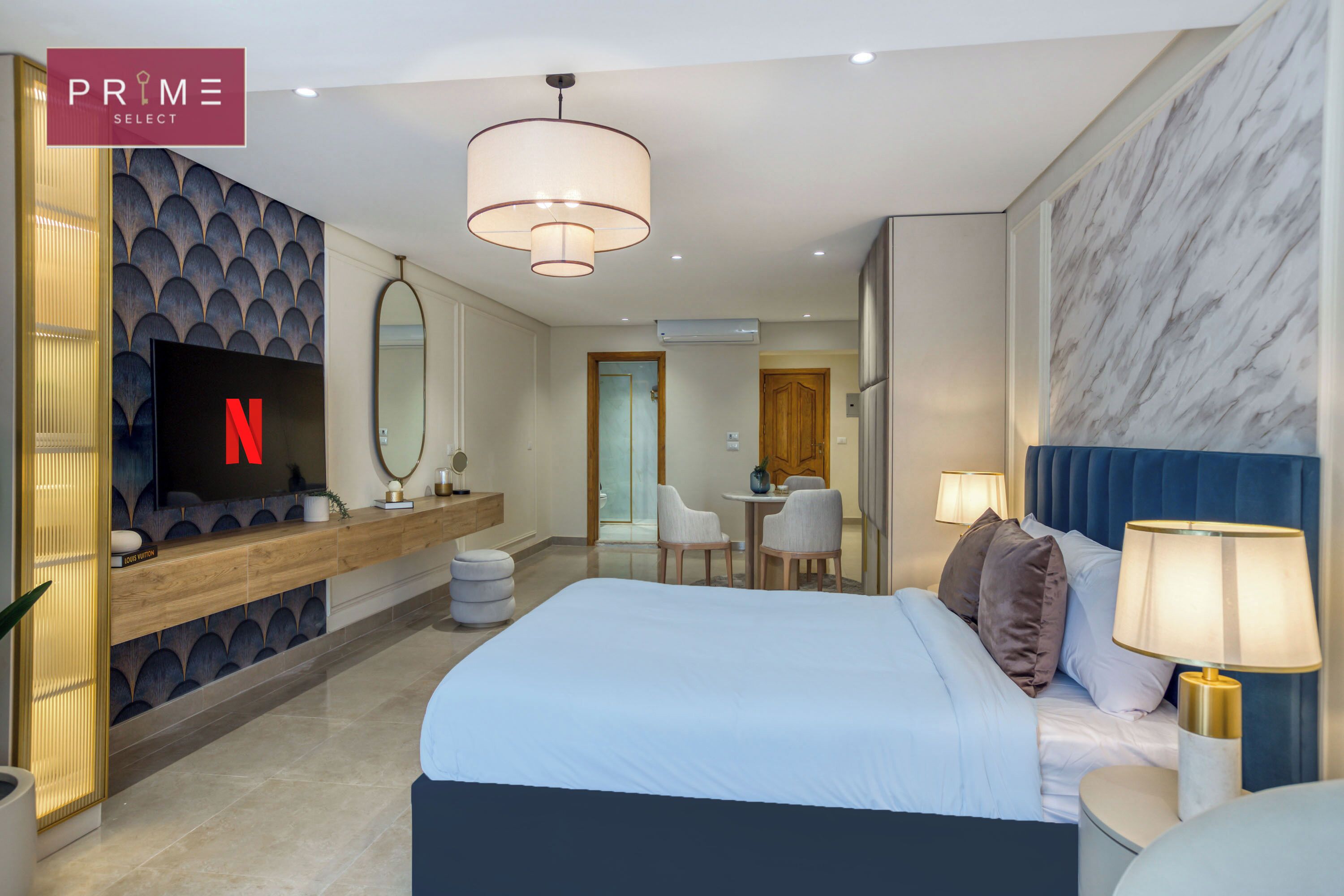 Una habitación de hotel moderna con una cama grande, un televisor montado en un mueble de madera, una zona de estar con sillas y una pared de mármol.