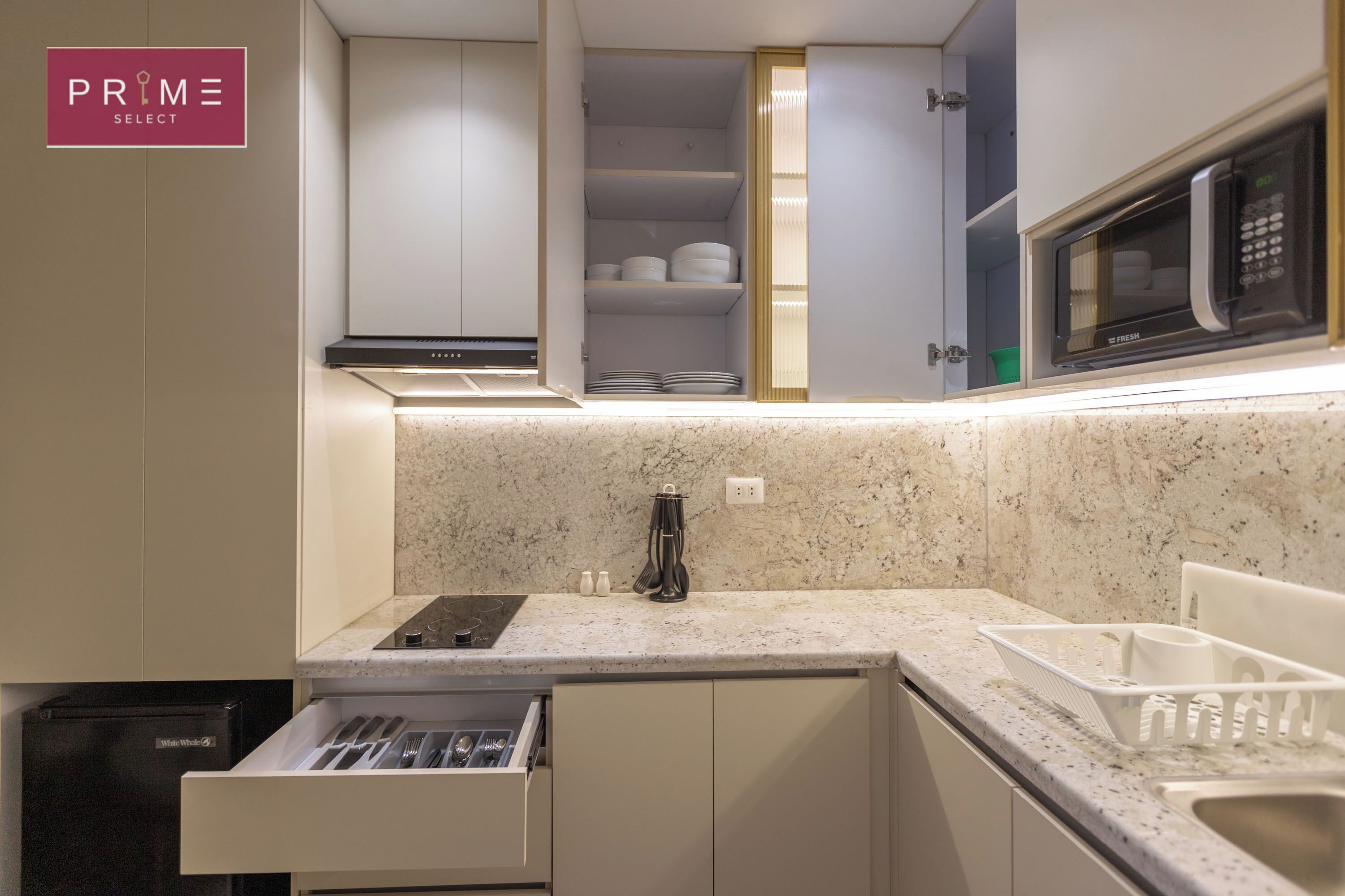 A modern kitchen with a built-in microwave, a dish rack, and a drawer with utensils.