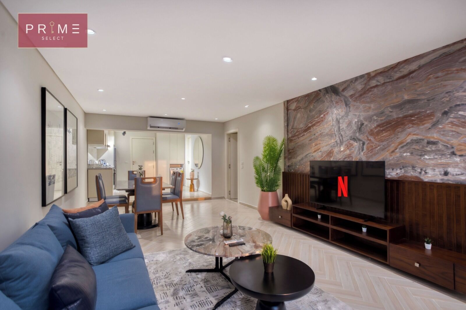 A modern living room with a blue sofa, a coffee table, and a TV mounted on a marble wall.