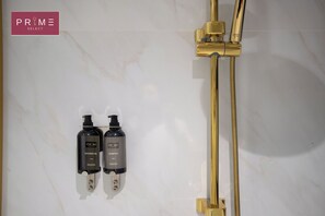 A bathroom with a gold shower system and two bottles of PRIME SELECT shower gel and shampoo. -  Prime Residence Arkadia (Cairo)