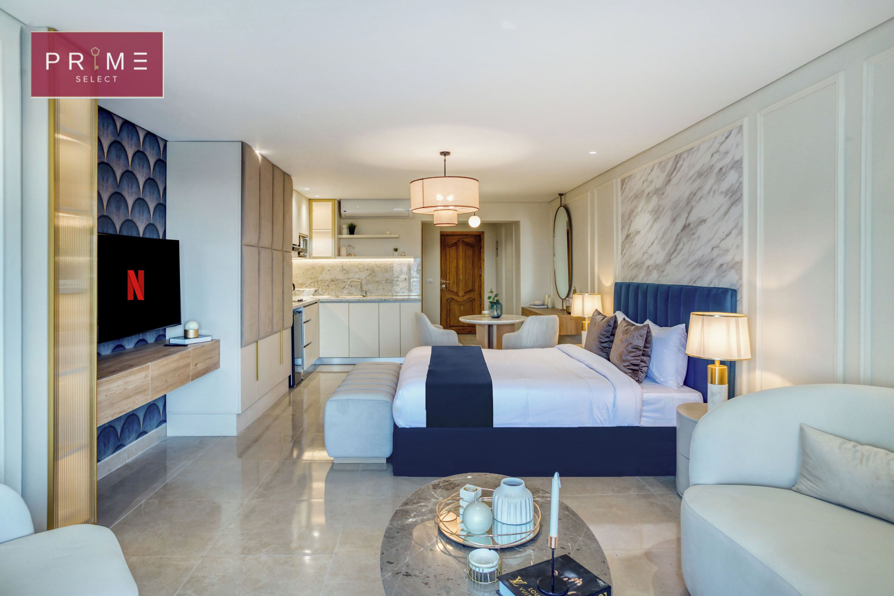 A modern hotel room with a large bed, a TV, a dining area, and a kitchen in the background.